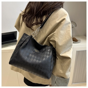 Detail of black quilted tote bag featuring gold chain straps and brand plate on a model
