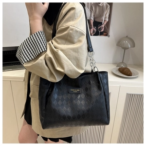 Detail of black quilted tote bag with silver chain strap shown on a model's shoulder