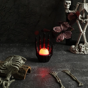 Macro view of Halloween skeleton hand holding a red glowing eyeball lamp with bloodshot detail