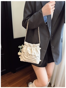 Detail of white quilted drawstring bucket bag with gold chain and tulip charm