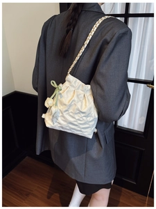 Detail of white quilted chain bag featuring gold hardware and a decorative green floral ribbon