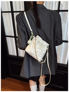 Close-up of beige quilted crossbody bag with gold chain and tulip charm detail