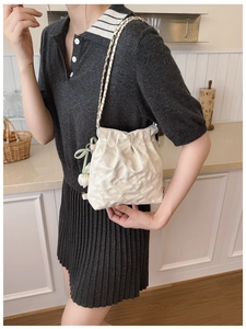 Detail of quilted bucket bag with chain strap and green ribbon shown in a home setting