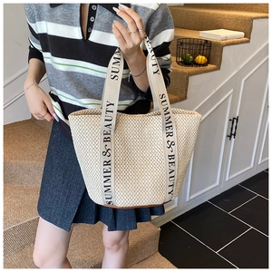 Close-up of woven straw tote bag with wide logo straps and detailed fiber texture