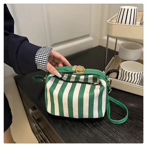 Detail view of striped canvas crossbody bag with green leather strap and gold metal buckle