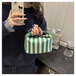 Close-up of green and cream striped canvas handbag with leather handle in hand