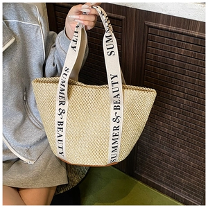 Detail of hand-woven straw bucket bag featuring logo straps and durable leather base