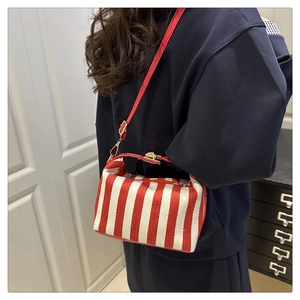 Detailed side view of a red striped canvas pillow bag with leather strap on a model