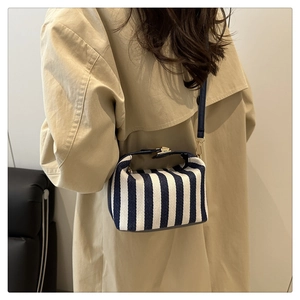 Detail of blue and white striped canvas boston bag styled with a khaki trench coat