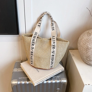Sac seau en paille avec poignées en toile Summer & Beauty posé sur une valise