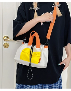 Detail of color-block nylon bucket bag showing drawstrings and bright orange handle