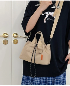 Detail view of a beige drawstring tote bag with an adjustable strap and side brand tag