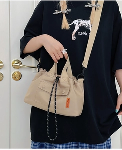 Detail of khaki nylon crossbody bag with orange logo tag and woven drawstring closure