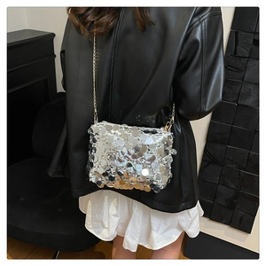 Detail of silver sequined handbag with gold chain strap worn over white skirt