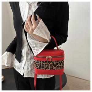 Detail of red leather and leopard print cylinder bag with dual gold zippers and top handle