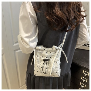 Detail of white quilted crossbody bag with black floral embroidery and drawstring closure