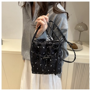 Detail of black quilted handbag with white bow patterns and adjustable drawstring closure