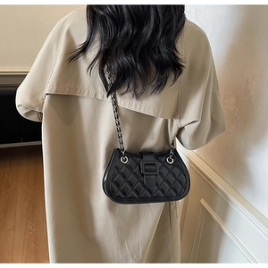 Dettaglio della borsa trapuntata nera con catena indossata su un classico trench color kaki