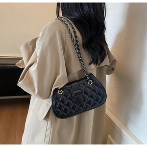 Detail of black quilted crossbody bag with metal chain strap worn over a beige trench coat