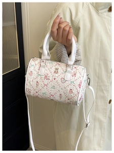 Detail of white cylindrical bucket bag with floral teddy bear print and leather handles