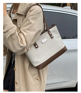 Detail of off-white woven tote bag with dark brown leather trim and silver brand plate