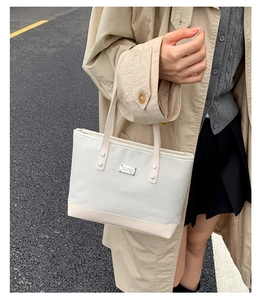Dettaglio della borsa tote tessuta crema con placca logo e finiture in pelle liscia