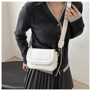 Detail of white crossbody bag featuring curved quilting and wide fabric shoulder strap