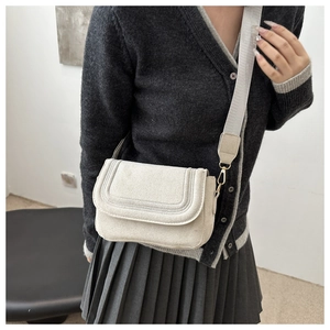 Detail of beige suede crossbody bag with wide fabric strap and gold hardware on model