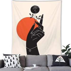 Artistic wall tapestry showing a hand holding flowers under a red sun above a sofa
