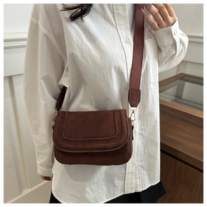Detail of vintage brown suede crossbody bag with decorative stitching and wide woven strap