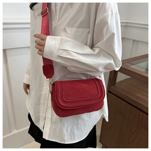 Detail of red suede flap bag featuring U-shaped stitching and wide adjustable fabric strap