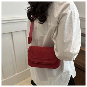 Detail of red suede crossbody bag with wide shoulder strap and modern flap closure