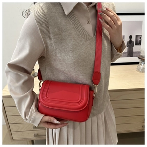 Detail of red leather crossbody bag with wide fabric strap and golden metal buckle