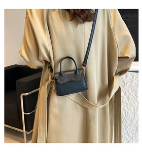 Détail du mini sac à main noir en cuir grainé porté par un mannequin en studio