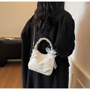Detail of white pleated handbag with bow and lace ribbon on a black coat background