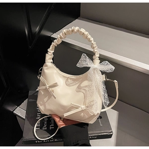 Close-up of creamy white pleated cloud bag with lace bow detail and slim shoulder strap