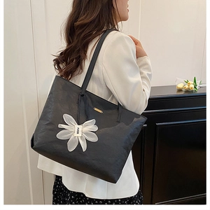 Detail der schwarzen Leder-Shopper mit weißem Blumenanhänger und goldener Metallplakette