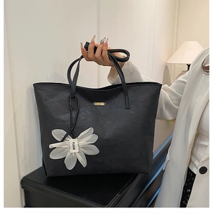 Détail d'un sac cabas plissé noir avec plaque dorée et pendentif floral élégant