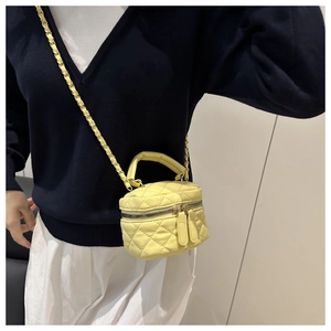 Detail of yellow quilted mini bag with gold chain strap and top handle on a model