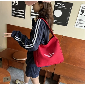 Side view of a red canvas tote bag with C'est la vie text worn by a model in a retro room