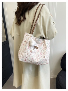 Close-up of floral tote bag with bear pattern, woven brown straps and plush pompom