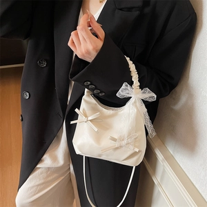 Chic beige pleated cloud bag with lace bow and crossbody strap on a black suit