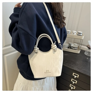 Detail of white marble-textured bucket bag with braided handle and gold metal hardware