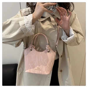 Detail of light pink bucket bag with knot handle and gold lettering on synthetic leather