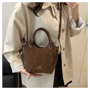 Détail d'un sac seau en cuir froissé marron foncé avec logo doré sur trench-coat beige