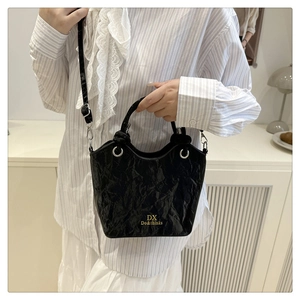 Detail of black wrinkled bucket bag with gold lettering shown on shoulder with strap