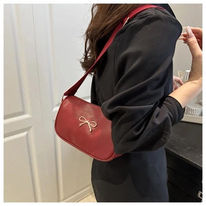 Detail of red baguette bag with golden bow ornament and wide fabric shoulder strap
