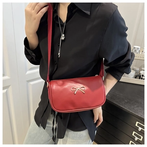 Detail of red crossbody square bag with golden bow buckle and wide fabric shoulder strap