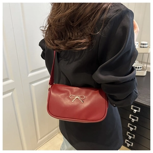 Detail of red leather shoulder bag featuring a gold bow clasp and sleek shoulder strap