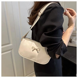Detail of white underarm bag featuring a golden metal bow and wide fabric shoulder strap